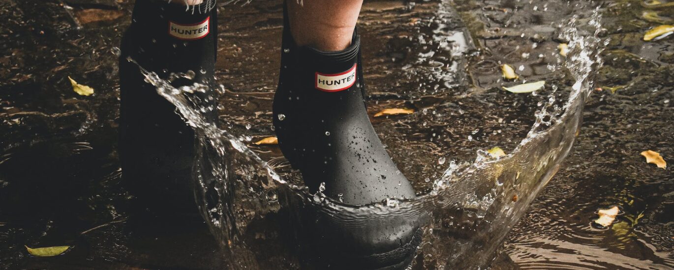 person in black rain boots walking on flooded ground