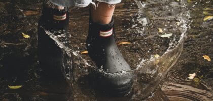 person in black rain boots walking on flooded ground